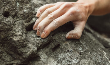 Woman climbing on rock outdoor, close-up image of climber hand in magnesium powder