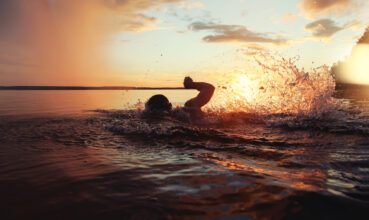 Athletic man is trained to swim in a lake at sunset. It flies a lot of water splashing. Vintage color