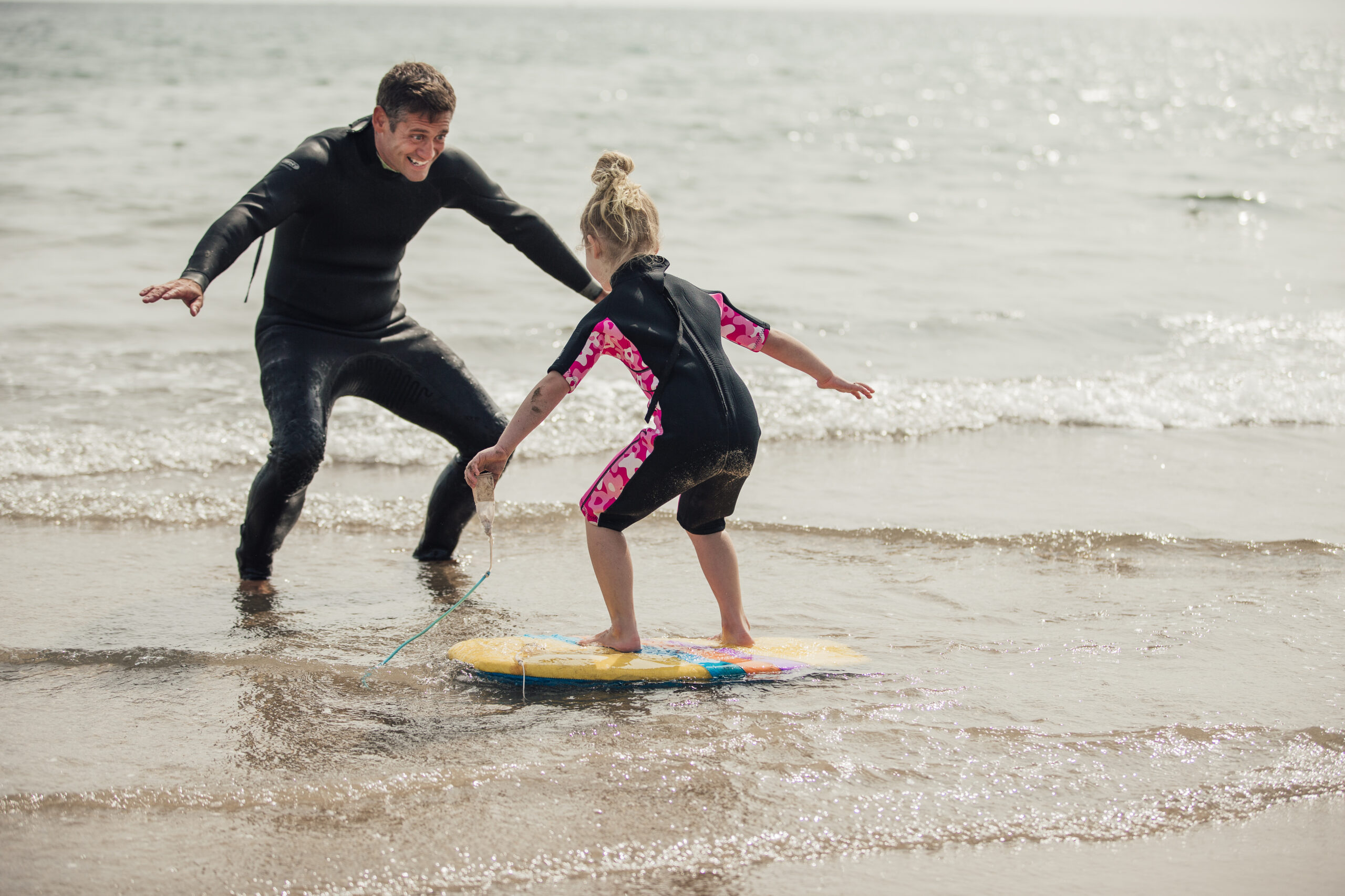 Mid adult male teaching a little girl how to surf at the beach.
