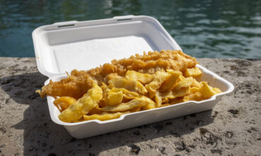 Fish and chips served in a polystyrene carton, placed on a harbour