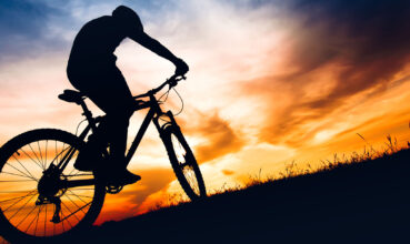silhouette of biker boy riding mountain bike on hills at sunset