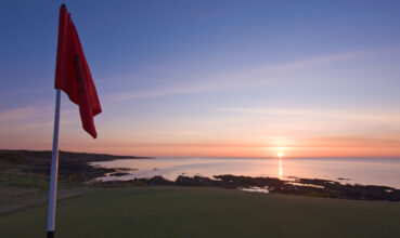 Red-golf-flag-on-a-coastal-course-at-sunrise