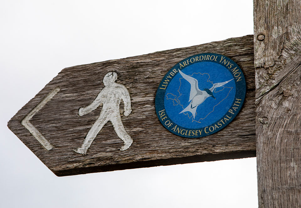 A sign pointing people to the direction of the Isle of Anglesey Coastal Path in North Wales, UK