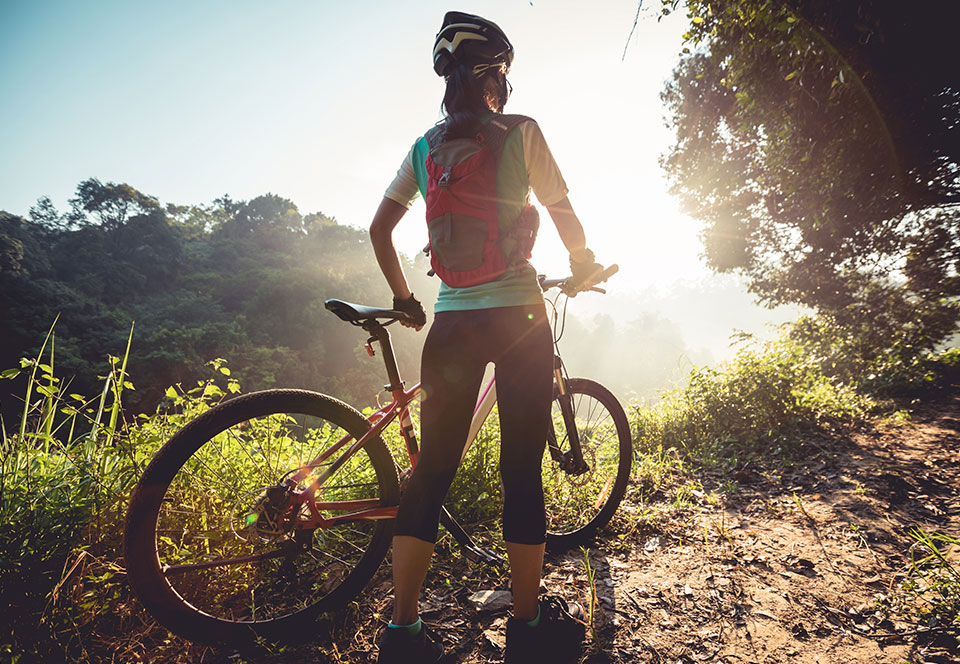 Young woman cyclist enjoy the beautiful sunrise on summer forest trail